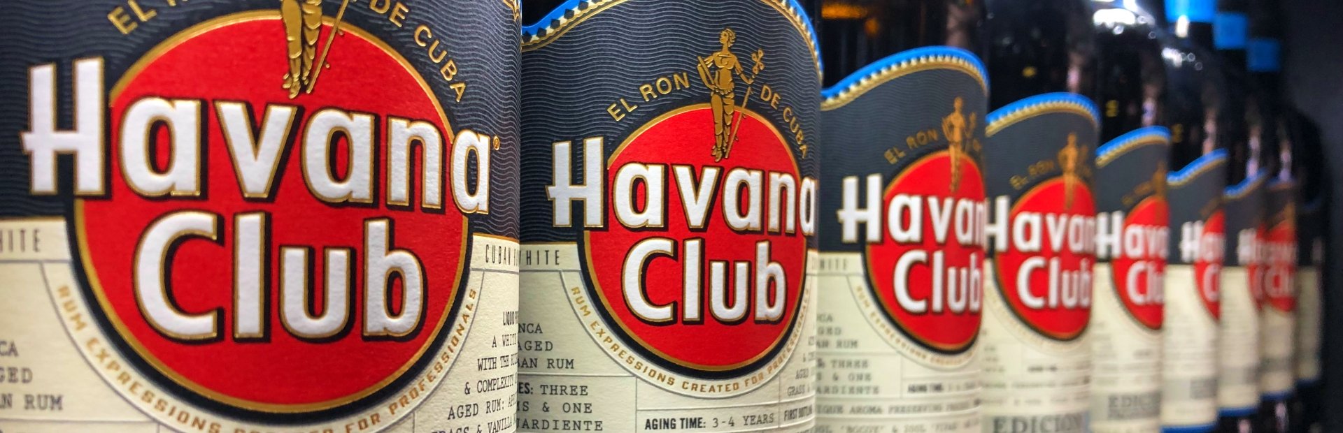 Rij Havana Club rumflessen in Cuba met verschillende labels en kleuren op een plank