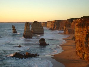 Rotsformaties en hoge kliffen langs een zandstrand bij zonsondergang in Australië