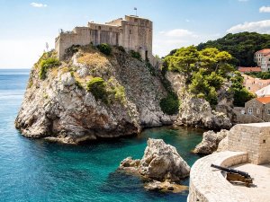 Middeleeuws stenen fort op een rotsachtige klif met uitzicht over een helder turquoise baai en een kanon op een stenen muur op de voorgrond in Kroatië