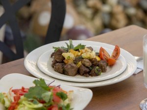 Bord met stukjes vlees en aardappelen in Gjirokastër in Albanië met tomaat, salade en een glas op een houten tafel