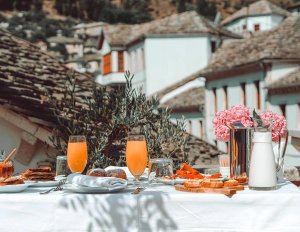 Buitenontbijt in Albanië met sinaasappelsap en gebak met uitzicht op een stad met traditionele stenen daken