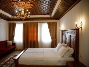 Slaapkamer in Albanië met groot houten bed, rijk bewerkt houten plafond met kroonluchter en een rode bank