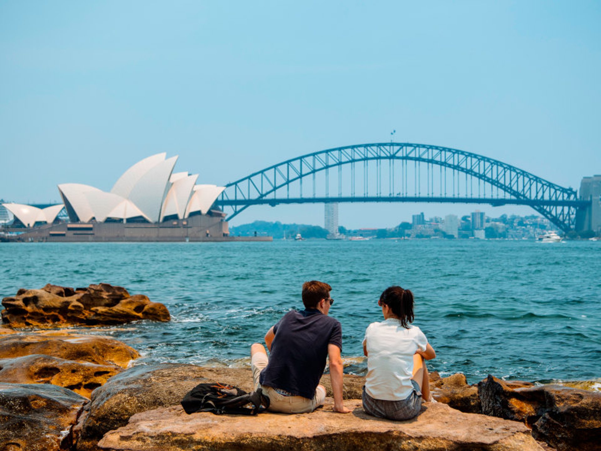 Twee mensen zitten op rotsen en kijken over het water naar het Sydney Opera House en de Harbour Bridge in Sydney Australië