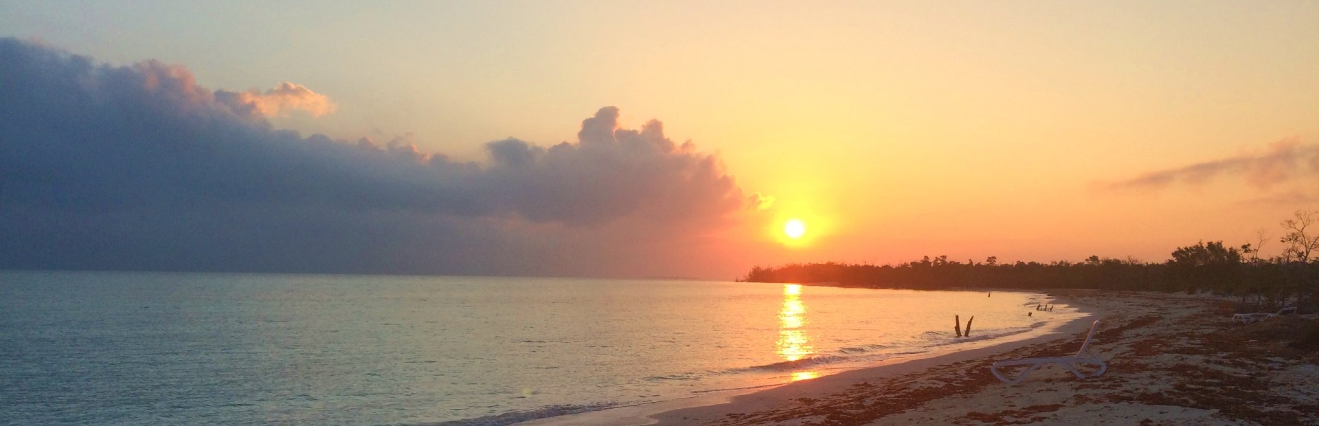 Gouden zonsondergang boven een rustige zee en zandstrand met wolken en reflectie van de zon op het water in Cuba