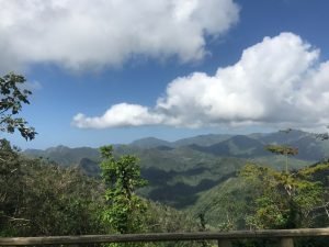 Weelderige groene bergen en valleien onder een blauwe lucht met verspreide witte wolken bij Baracoa in Cuba