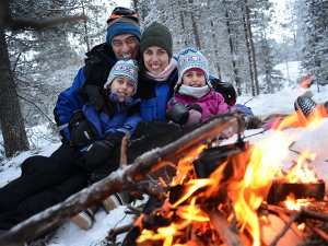 Een lachend gezin van vier zit bij een kampvuur in een besneeuwd bos in Lapland.