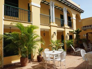 Binnenplaats met gele gebouwen, balkons, palmbomen in potten en wit metalen tuinmeubilair in Cuba