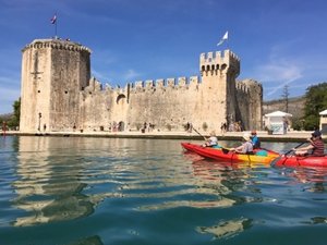 Kayakers paddle on water in front of a historic stone fortress.