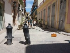 Zonnige voetgangersstraat met kleurrijke gebouwen, een ketting tussen twee donkere paaltjes en mensen verderop in Havana in Cuba
