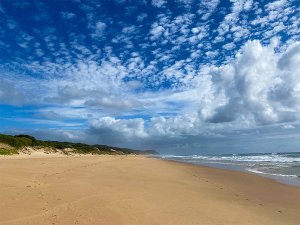 Uitgestrekt, leeg zandstrand met de zee rechts en een helderblauwe lucht vol witte wolken.