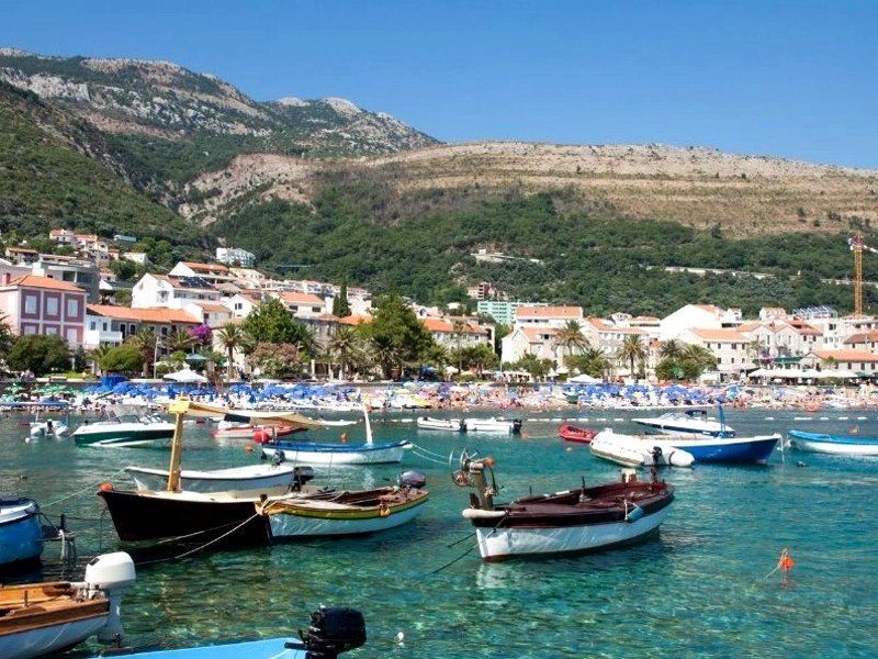Kleine boten in helder turquoise water bij een druk strand en kustplaats aan de voet van de bergen in Kroatië