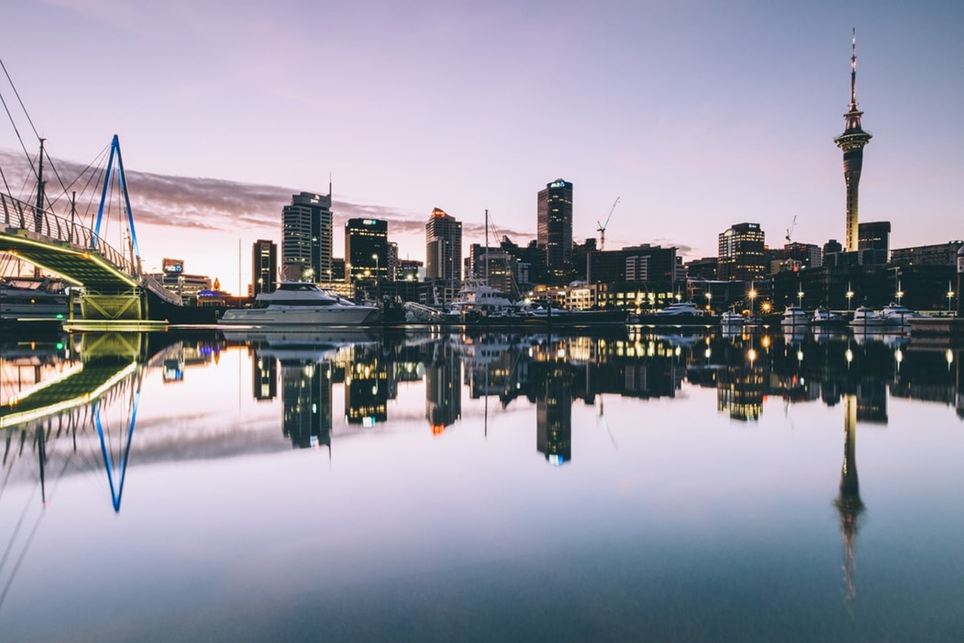 Stads skyline bij schemering weerspiegelt in kalm water met een hoge toren en verlichte brug aan de kust