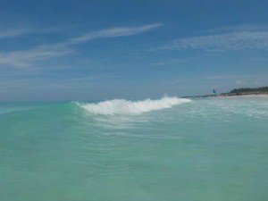 Een enkele golf breekt op turquoise zeewater onder een heldere blauwe lucht met een verre kustlijn bij Varadero in Cuba
