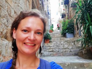Lachende vrouw maakt selfie in smalle stenen steeg in Kroatië met trappen en planten in potten