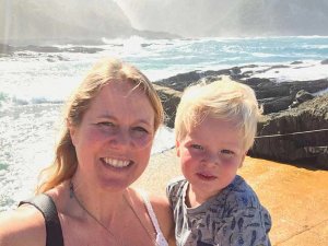 Vrouw en jong kind lachen op een zonnige, rotsachtige kust met golven van de oceaan in Zuid-Afrika