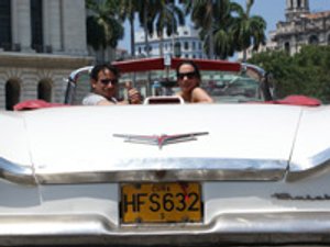 Glimlachende man geeft duim omhoog naast vrouw in witte klassieke cabrio op straat in Havana Cuba