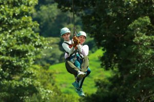 Een volwassene en een kind lachen terwijl ze samen aan een zipline door het bos gaan in Costa Rica.