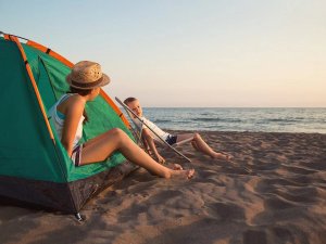 Twee mensen ontspannen bij een groene tent op een zandstrand met uitzicht op zee tijdens zonsondergang in Kroatië