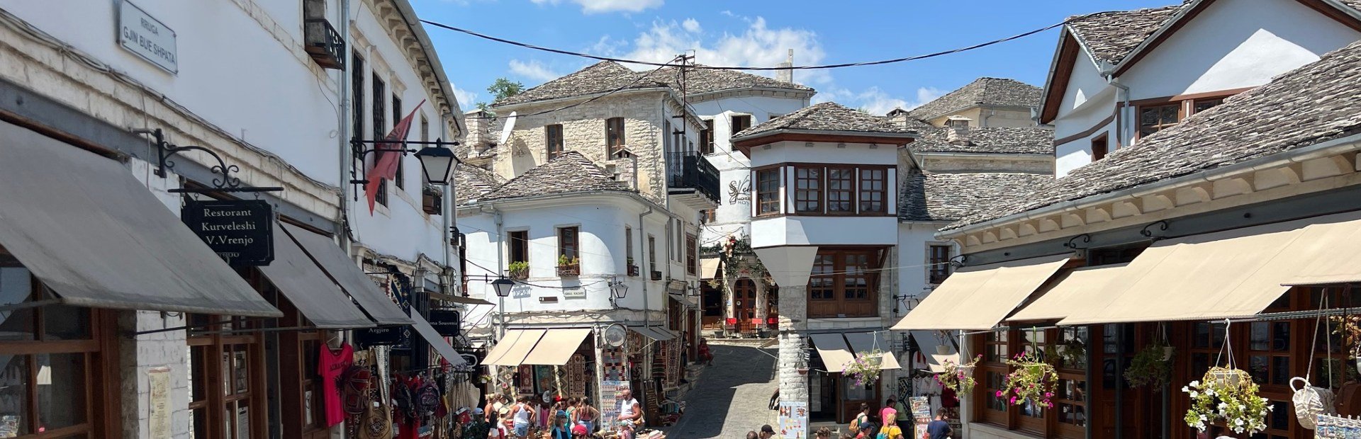 Levendige historische straat in Gjirokastër in Albanië met witte stenen huizen, grijze pannendaken en winkels met luifels
