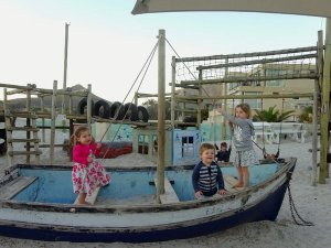 Drie jonge kinderen spelen in een blauwe boot gevuld met zand op een zanderige buitenspeelplaats in Zuid-Afrika