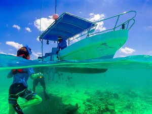 Kind snorkelt onder boot met blauw zeil in helder turquoise water.