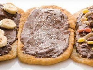 Drie stukken gefrituurd deeg belegd met chocoladespread, één met banaan, één met gekleurde snoepjes en één enkel met poedersuiker.